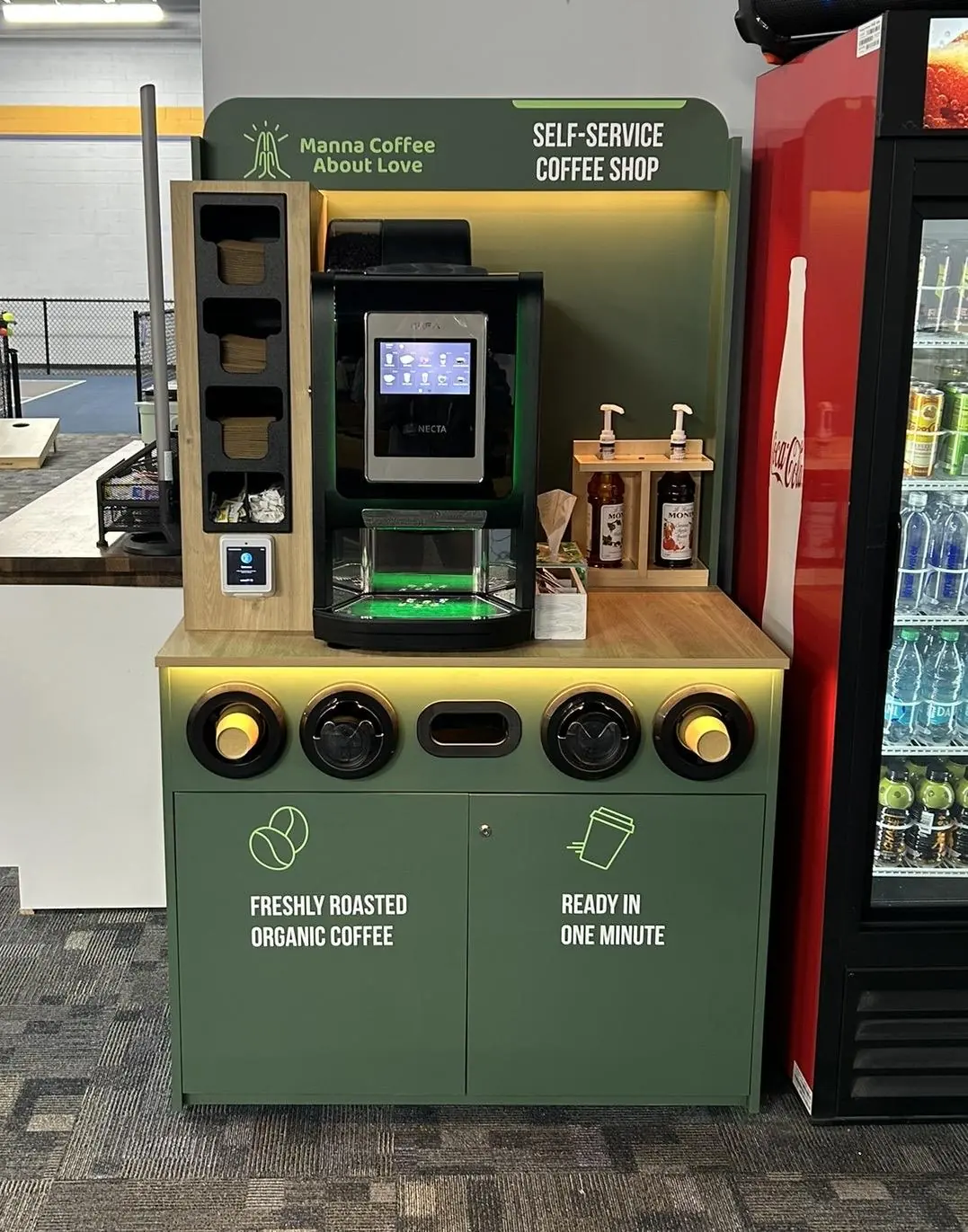 A Manna coffee kiosk on a retail floor beside a cold-drinks cooler